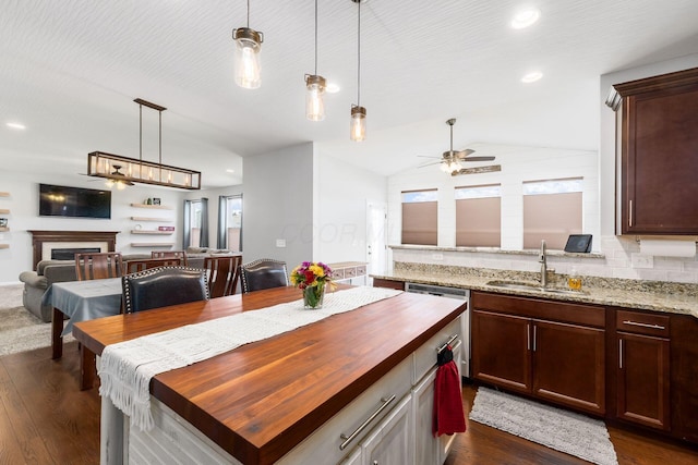 kitchen with butcher block countertops, dishwasher, a sink, open floor plan, and vaulted ceiling