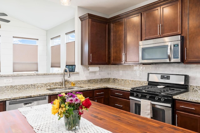 kitchen featuring lofted ceiling, butcher block countertops, stainless steel appliances, decorative backsplash, and a sink
