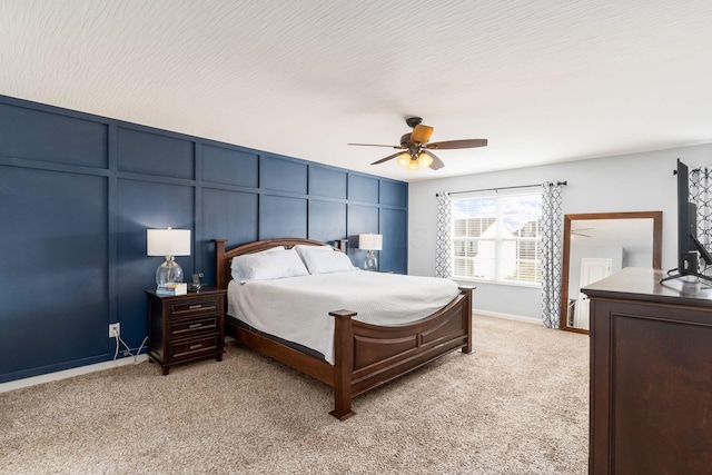 bedroom featuring a decorative wall, light carpet, baseboards, and ceiling fan