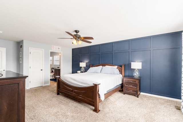 bedroom featuring a decorative wall, ensuite bathroom, light colored carpet, and ceiling fan