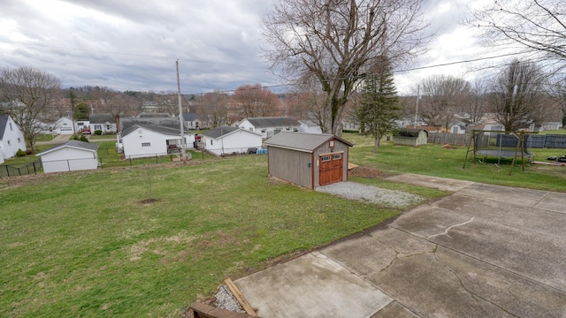 view of yard featuring a trampoline, a shed, a residential view, a fenced backyard, and an outdoor structure