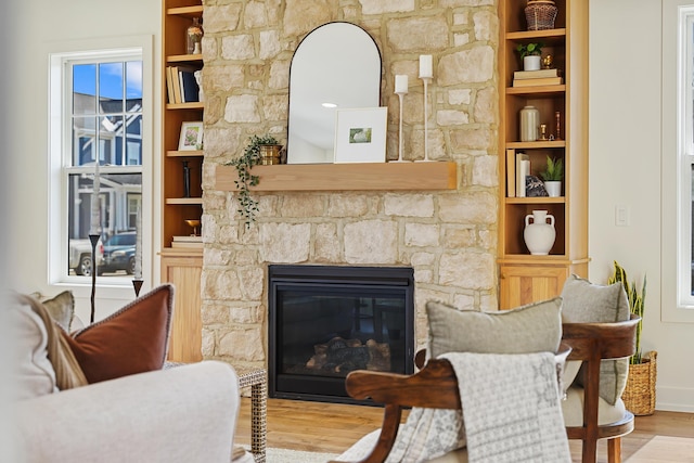 sitting room with a stone fireplace, built in shelves, and wood finished floors