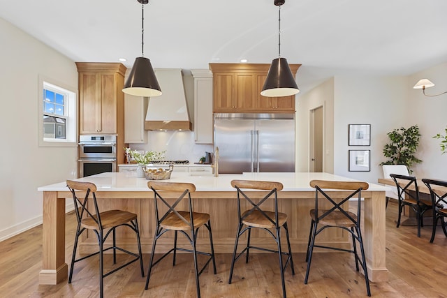 kitchen featuring a spacious island, light wood finished floors, light countertops, custom range hood, and appliances with stainless steel finishes