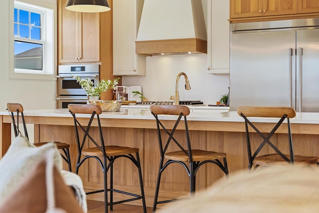 kitchen featuring a kitchen breakfast bar, appliances with stainless steel finishes, light countertops, and custom range hood