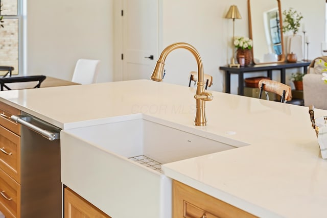 kitchen featuring brown cabinetry, a sink, light countertops, and stainless steel dishwasher