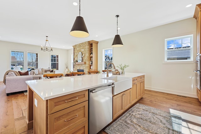 kitchen with stainless steel dishwasher, light countertops, light wood-style flooring, and a sink