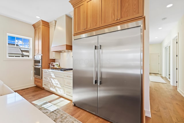 kitchen with light wood-style flooring, recessed lighting, stainless steel appliances, light countertops, and custom range hood
