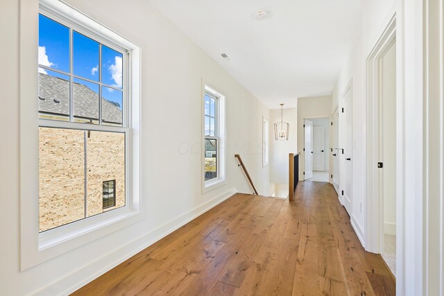 hall with an upstairs landing, light wood-type flooring, and baseboards