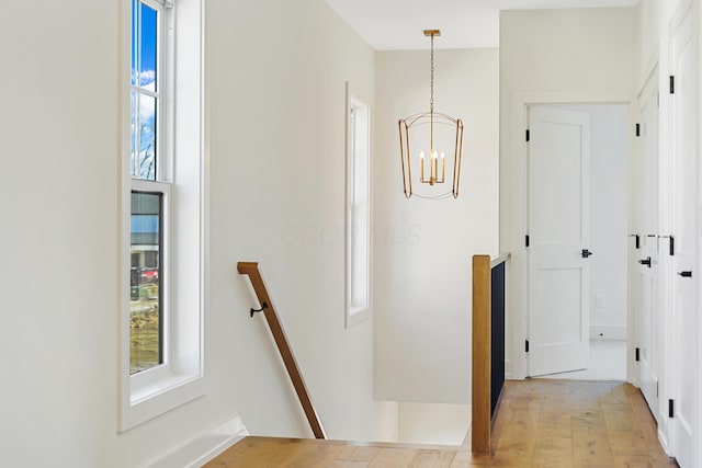hallway with light wood-style floors, an upstairs landing, and a notable chandelier