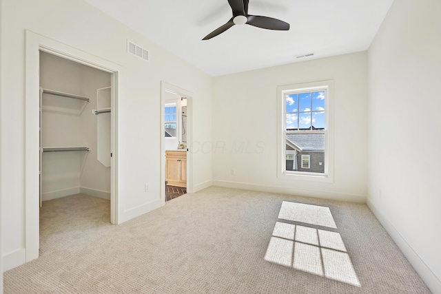 unfurnished bedroom with a walk in closet, carpet, visible vents, and baseboards