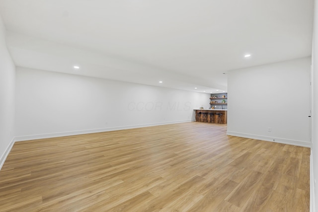 basement featuring light wood-style flooring, recessed lighting, baseboards, and a dry bar