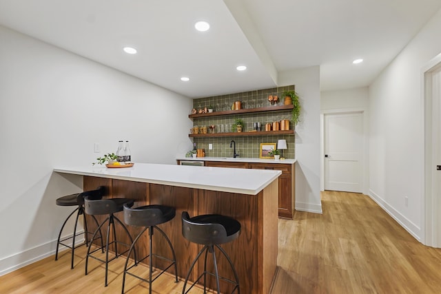 bar with light wood-type flooring, decorative backsplash, recessed lighting, indoor wet bar, and baseboards