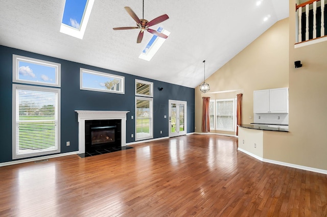 unfurnished living room featuring high vaulted ceiling, a skylight, a fireplace, a ceiling fan, and wood finished floors