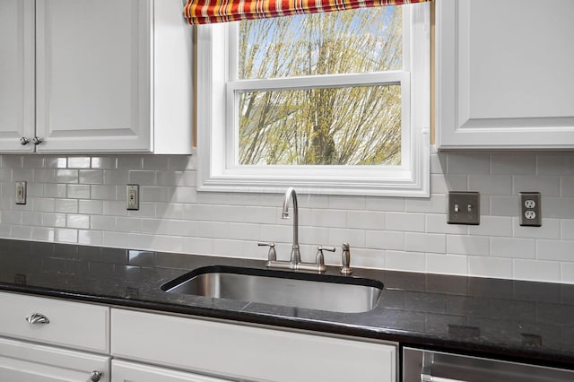 kitchen featuring a sink, white cabinets, decorative backsplash, stainless steel dishwasher, and dark stone countertops
