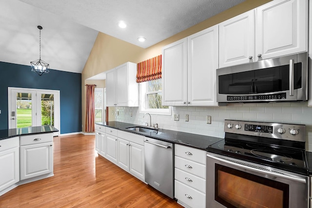 kitchen with stainless steel appliances, a sink, vaulted ceiling, dark countertops, and decorative backsplash