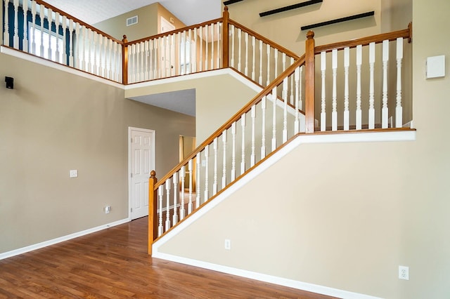 stairway with a high ceiling, wood finished floors, and baseboards