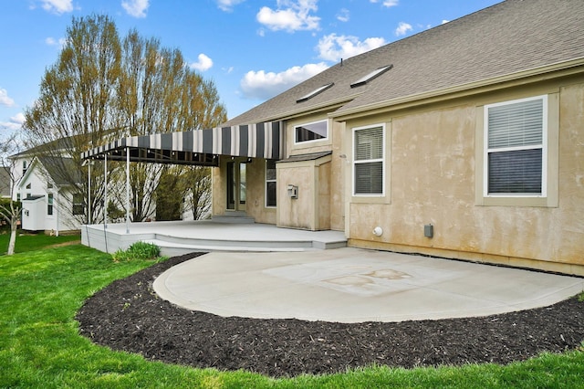 rear view of house featuring a patio area, a yard, roof with shingles, and stucco siding