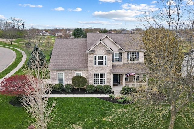 traditional-style house with stone siding, a front lawn, a shingled roof, and a porch