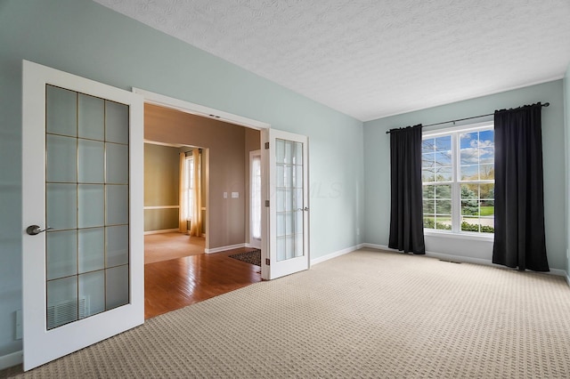 carpeted empty room featuring french doors, baseboards, a textured ceiling, and wood finished floors