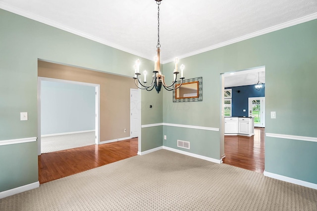 carpeted spare room featuring a chandelier, crown molding, baseboards, and wood finished floors