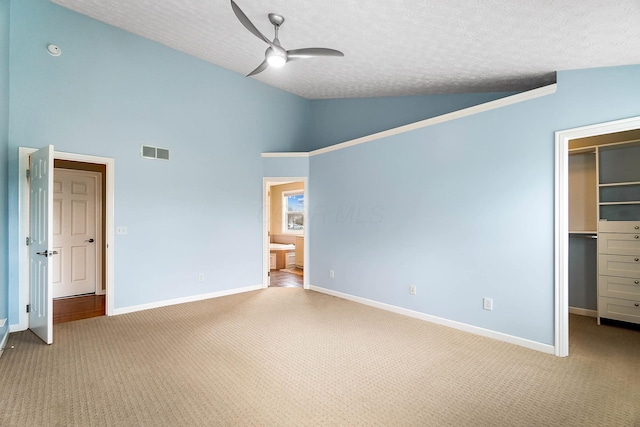 unfurnished bedroom featuring light colored carpet, a walk in closet, a textured ceiling, baseboards, and high vaulted ceiling
