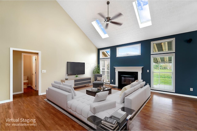 living room with high vaulted ceiling, a skylight, a fireplace with flush hearth, baseboards, and wood finished floors