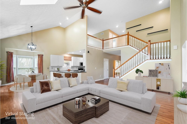 living room with light wood finished floors, high vaulted ceiling, ceiling fan, stairway, and baseboards