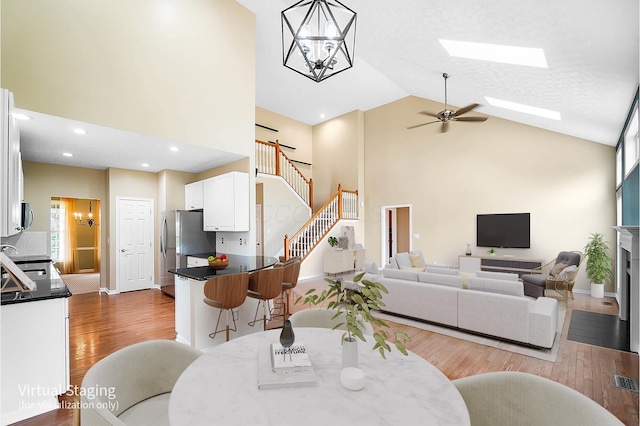 dining area with high vaulted ceiling, wood finished floors, ceiling fan, a chandelier, and stairway