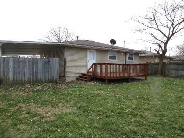 rear view of property with a lawn, a wooden deck, an attached carport, and fence
