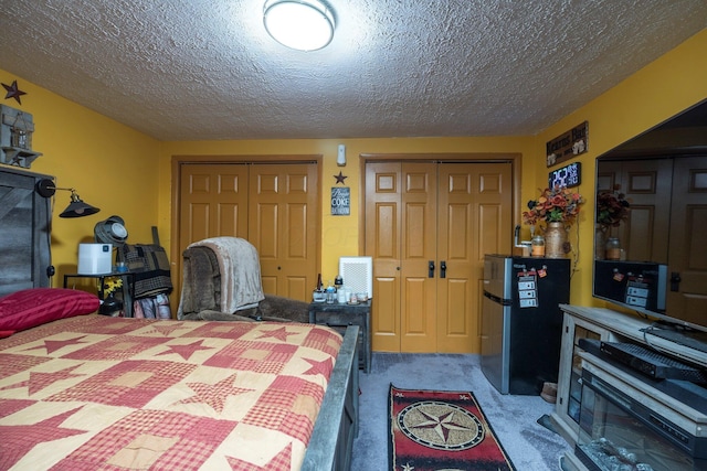 carpeted bedroom featuring a textured ceiling, freestanding refrigerator, and multiple closets