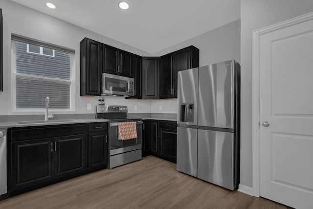 kitchen featuring light wood-style floors, dark cabinets, a sink, and stainless steel appliances