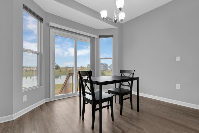 dining space with a water view, dark wood-style floors, baseboards, and a chandelier