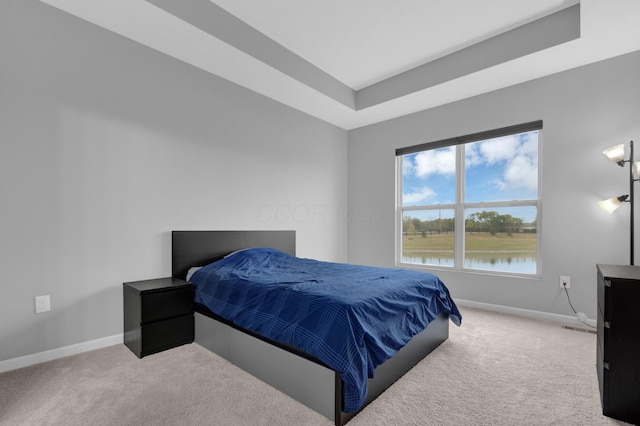 bedroom with carpet floors, a water view, baseboards, and a tray ceiling