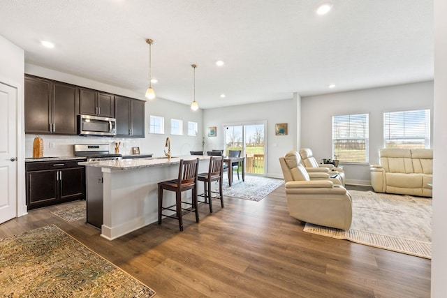 kitchen featuring tasteful backsplash, appliances with stainless steel finishes, open floor plan, dark wood-style flooring, and dark brown cabinets