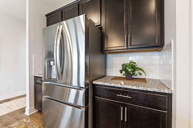 kitchen with dark brown cabinetry, tasteful backsplash, wood finished floors, light stone countertops, and stainless steel fridge