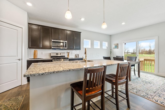 kitchen featuring light stone countertops, dark wood finished floors, tasteful backsplash, appliances with stainless steel finishes, and a sink