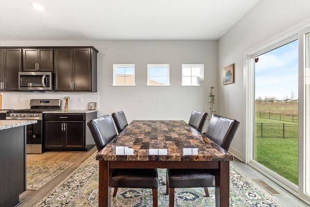 dining space with light wood-style flooring, plenty of natural light, and visible vents