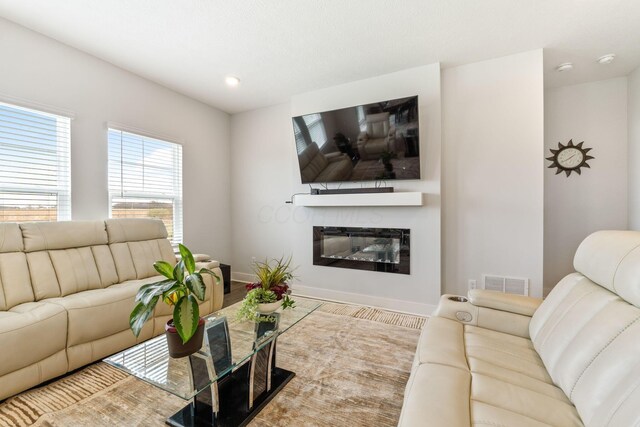 living room with wood finished floors, a glass covered fireplace, baseboards, and visible vents