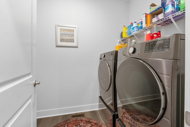 washroom featuring visible vents, baseboards, wood finished floors, laundry area, and washer and clothes dryer