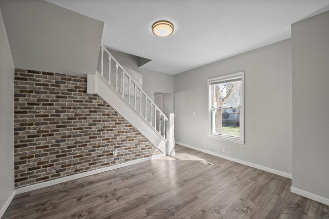 unfurnished living room with baseboards, stairs, wood finished floors, and brick wall
