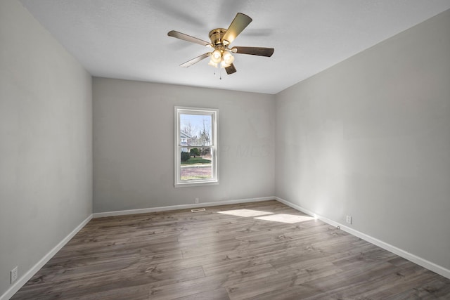 empty room featuring baseboards, wood finished floors, and a ceiling fan