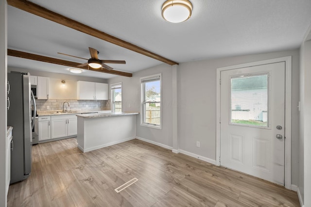 kitchen with white cabinets, light wood finished floors, stainless steel appliances, beam ceiling, and backsplash