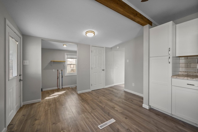 unfurnished living room featuring dark wood-style flooring, beam ceiling, baseboards, and visible vents