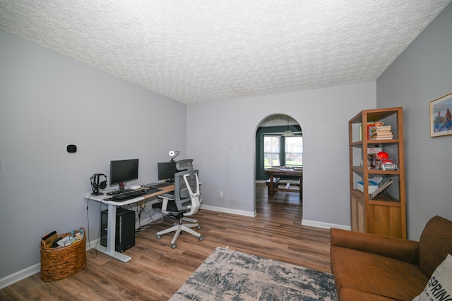 office featuring arched walkways, wood finished floors, baseboards, and a textured ceiling