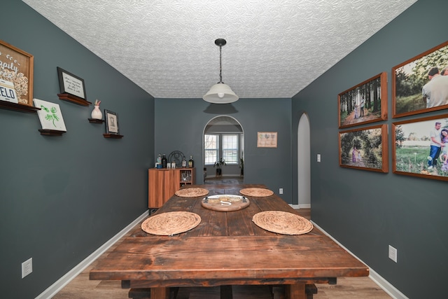 dining space featuring arched walkways, baseboards, a textured ceiling, and wood finished floors