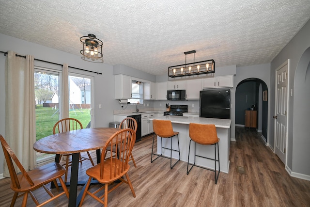 dining space with arched walkways, a textured ceiling, baseboards, and wood finished floors