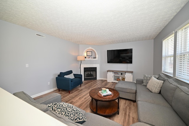 living area with a textured ceiling, wood finished floors, a fireplace, and visible vents