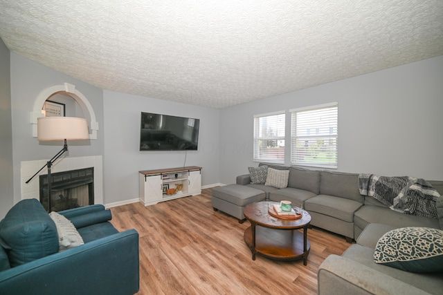 living area featuring a textured ceiling, light wood finished floors, a tiled fireplace, and baseboards
