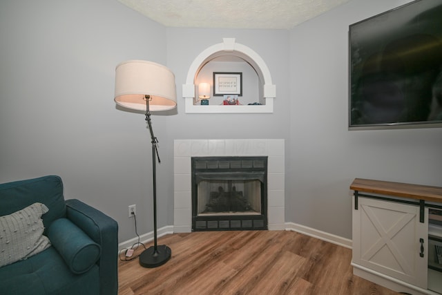 sitting room with baseboards, a tile fireplace, wood finished floors, and a textured ceiling