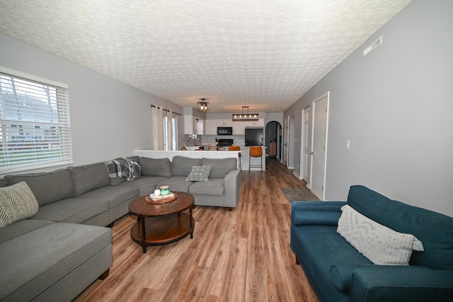 living area featuring a textured ceiling, wood finished floors, visible vents, and arched walkways